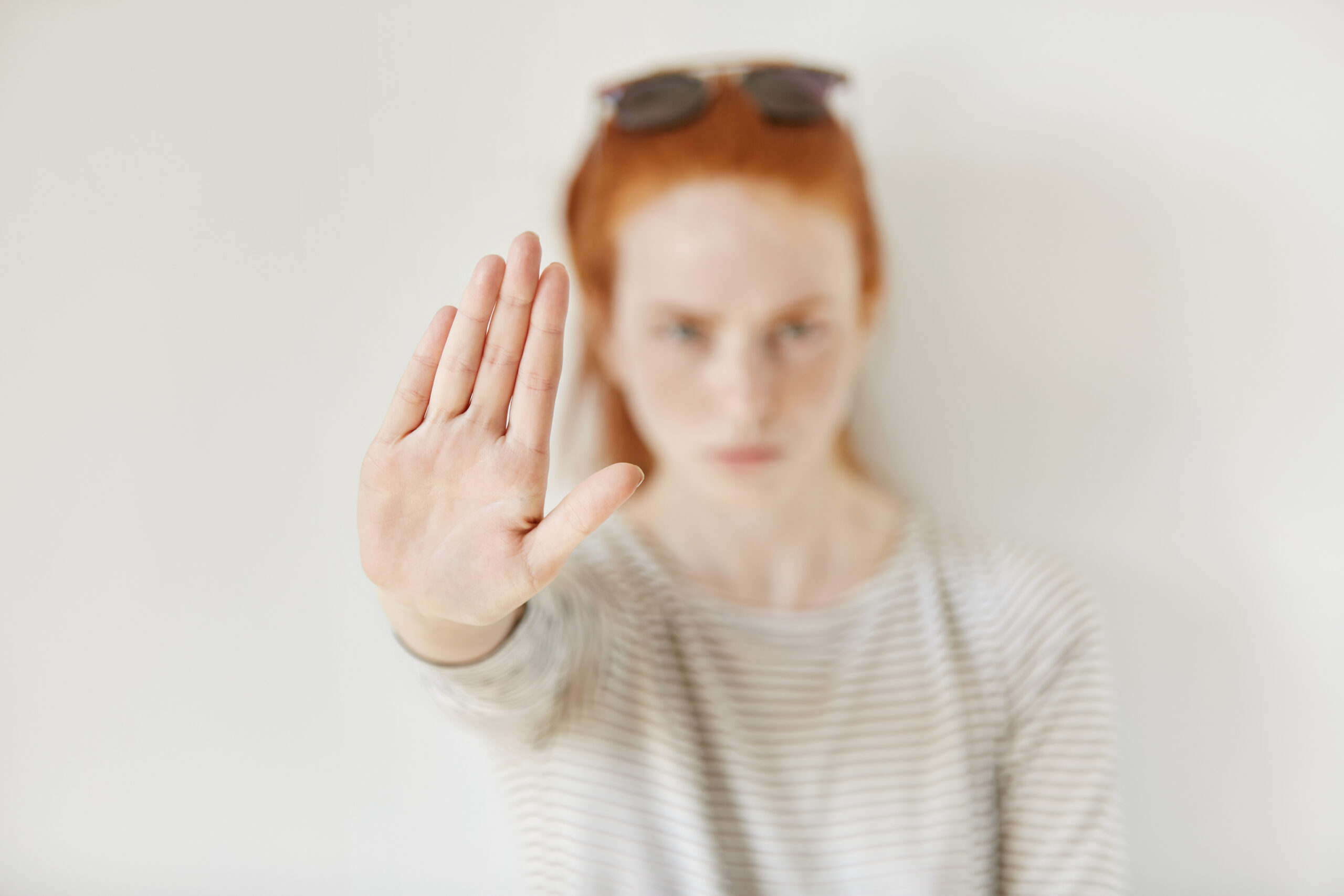 Young annoyed woman with bad attitude making stop gesture with her palm outward, saying no, expressing denial or restriction. Negative human emotions, feelings, body language. Selective focus on hand